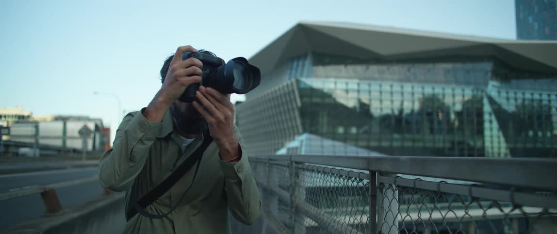 A male photographer taking pictures outside near a city building and chain link fence