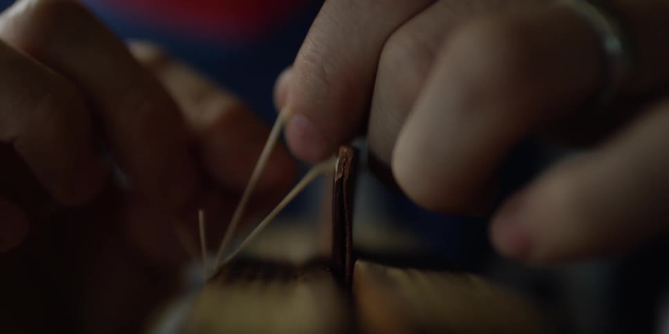 Hands use a needle to  sew material