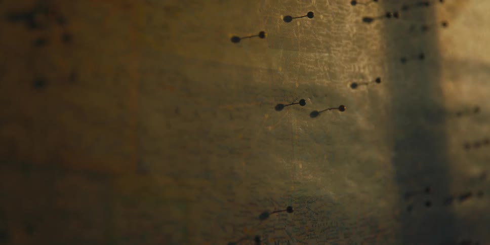 Person sticks pin into map full of pins with shadowed bar cast across its surface