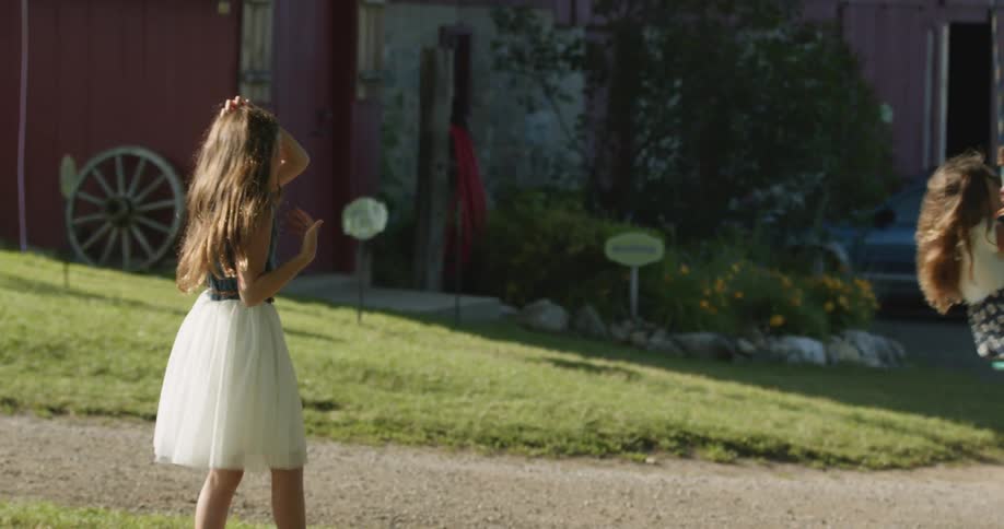 A girl pushes her little sister on a tire swing in their yard