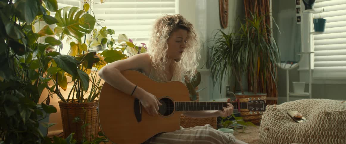 Young blonde woman playing acousting guitar on the living room at home