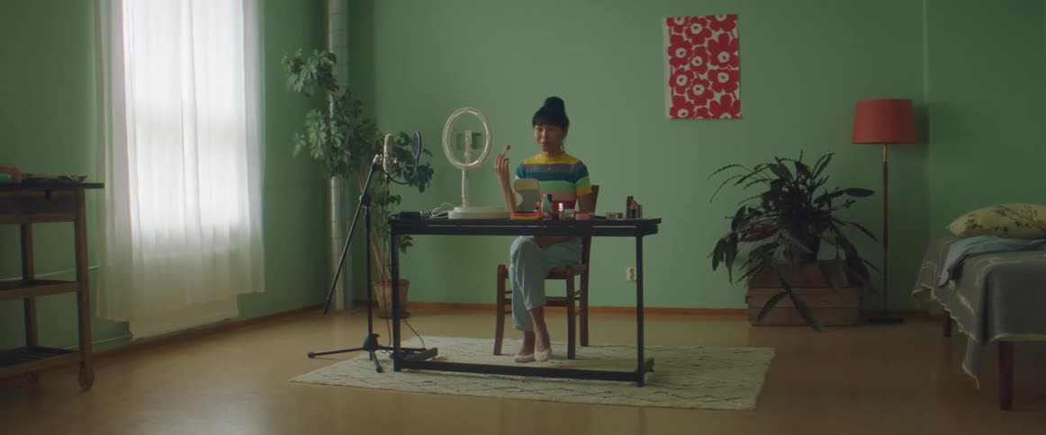 A woman sits at home and talks as she applies make up to her face