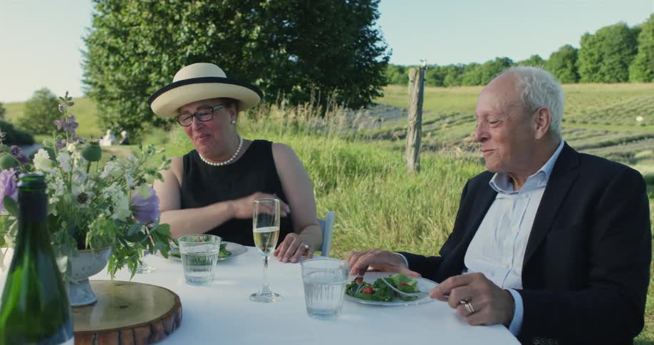 An older man and woman talking and laughing while dining outside at an event