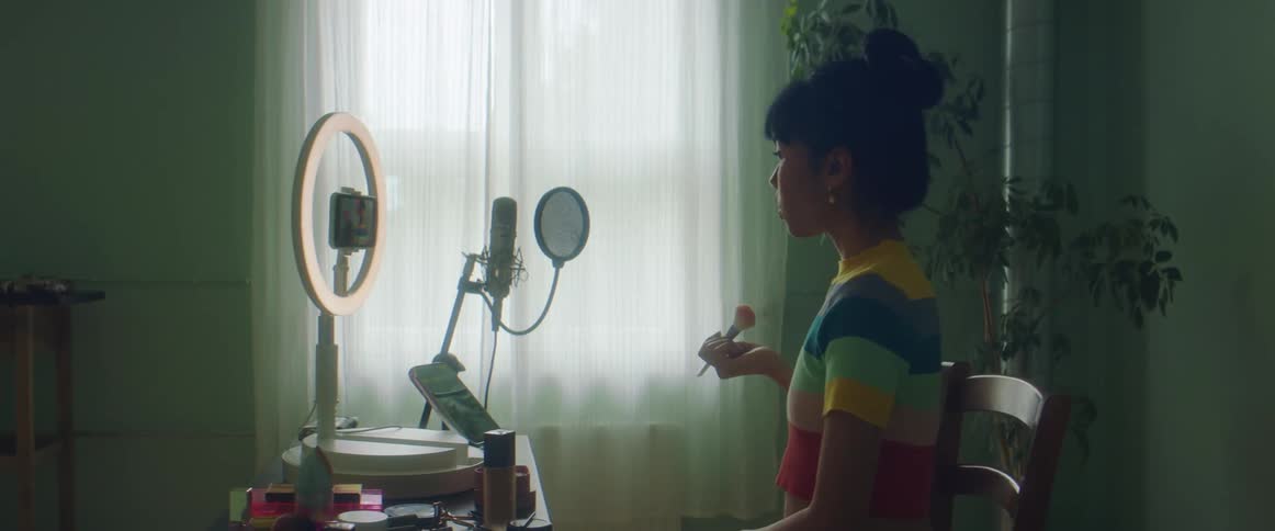 A woman sits in front of a mirror applying makeup