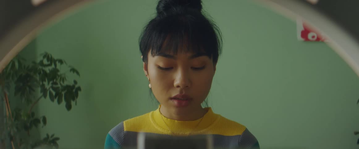 A young woman sitting in front of a mirror applies makeup to her face using a brush