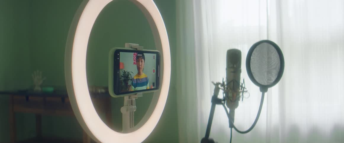 Woman films herself using mobile phone o ring light and a microphone while discussing makeup