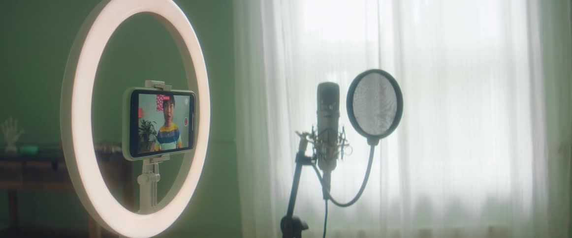 Woman touches a red record icon on a cell phone and records herself smiling and waving