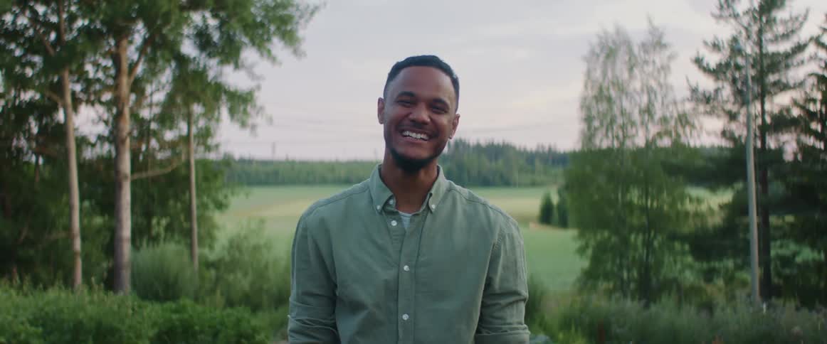Young man wearing a green shirt laughing while standing near a field at evening
