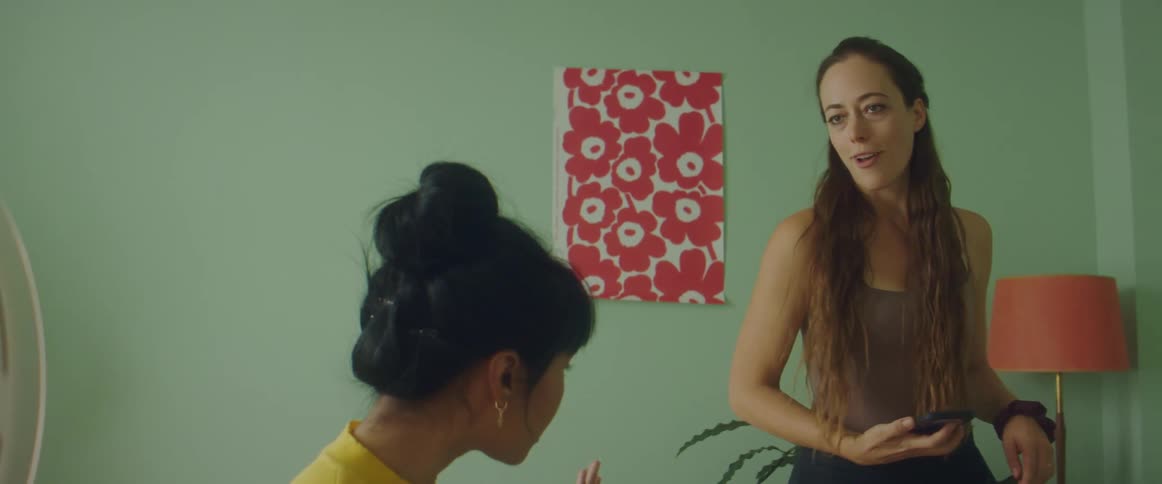 A woman doing makeup with a phone while another woman messes with them playfully