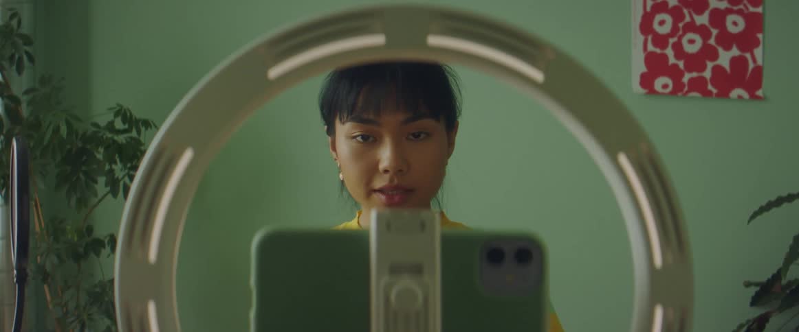 A woman in a room adjusting a smart phone on a ring light stand with a wall in the background
