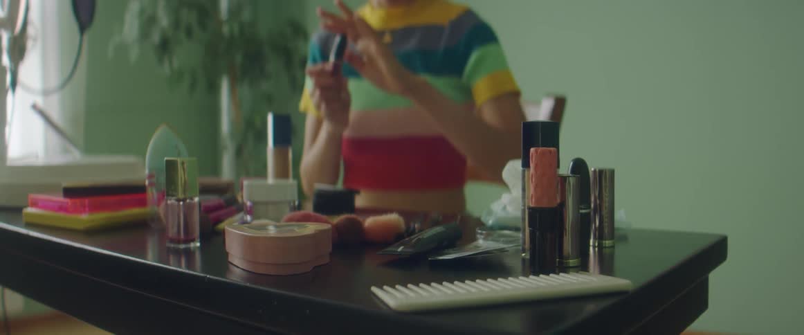 A woman is at a desk and picks up a lipstick