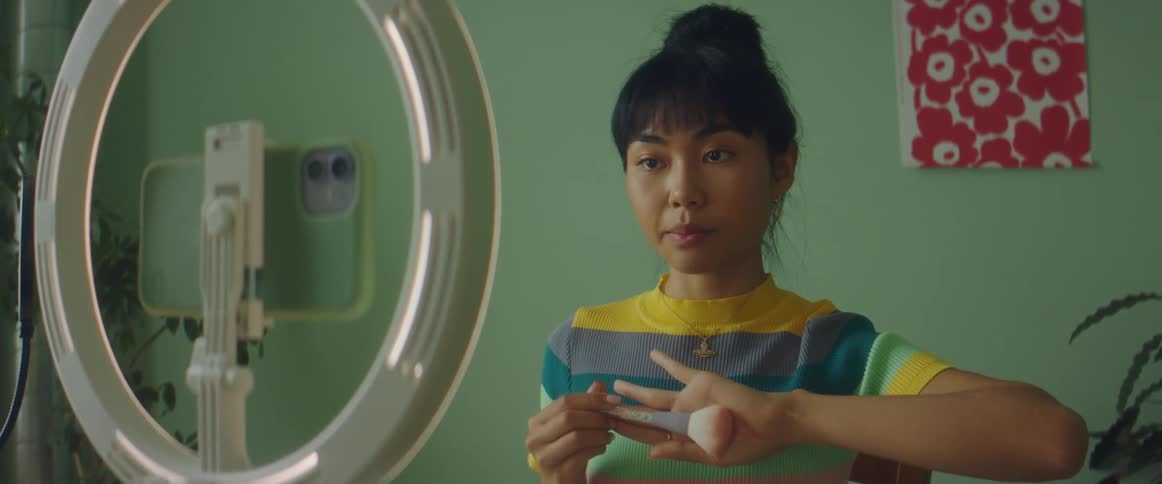 Young woman recording a video of herself applying makeup in a home studio