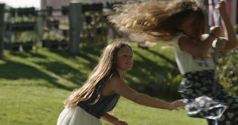 Two girls are outside with one on a swing and the other one pushing her