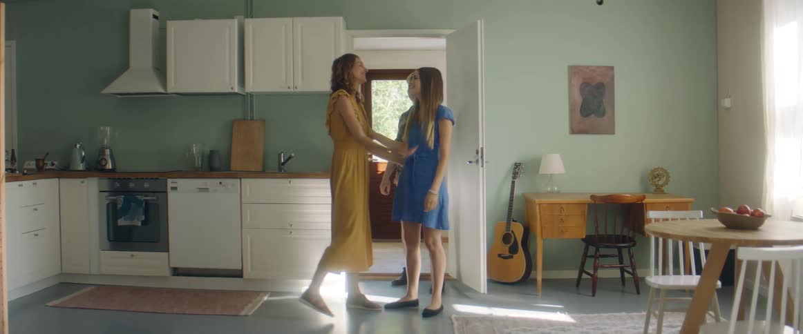 A woman greets another couple by hugging them as they walk into the kitchen