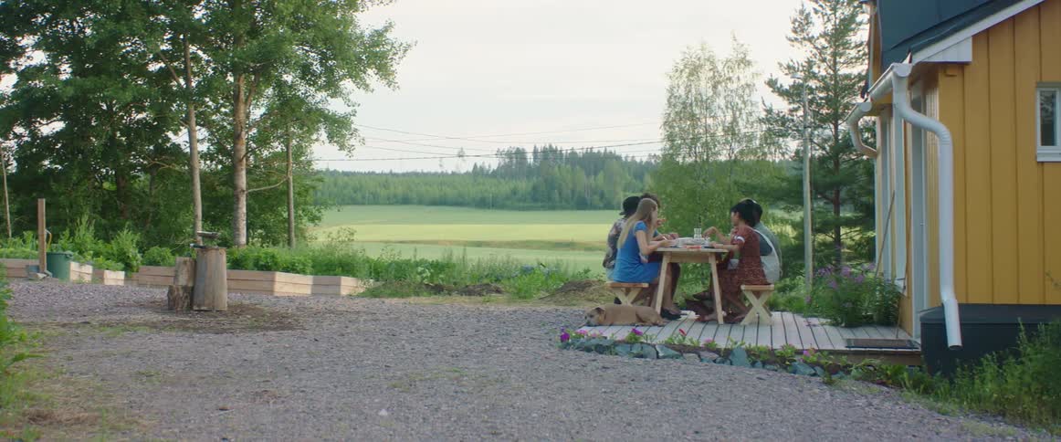 Group of friends sitting at a table on the backyard of a house on a rural area eating
