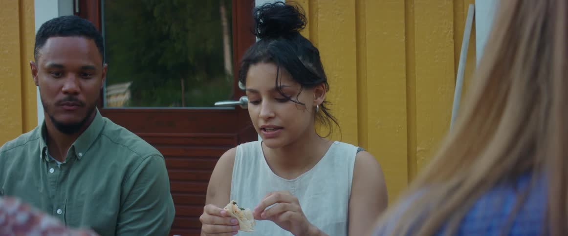 A group of friends sitting at table eats food and talks to each other outdoors