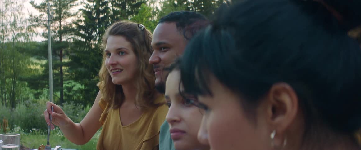 A group of friends talk as they eat in the garden at a barbecue
