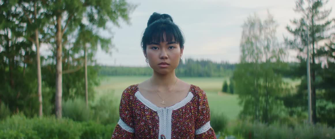 Woman with patterned dress faces the camera on the grass