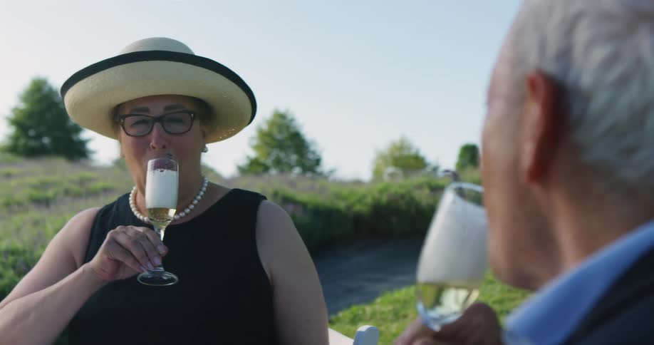 A man and woman sitting by a river toast one another as they drink champagne