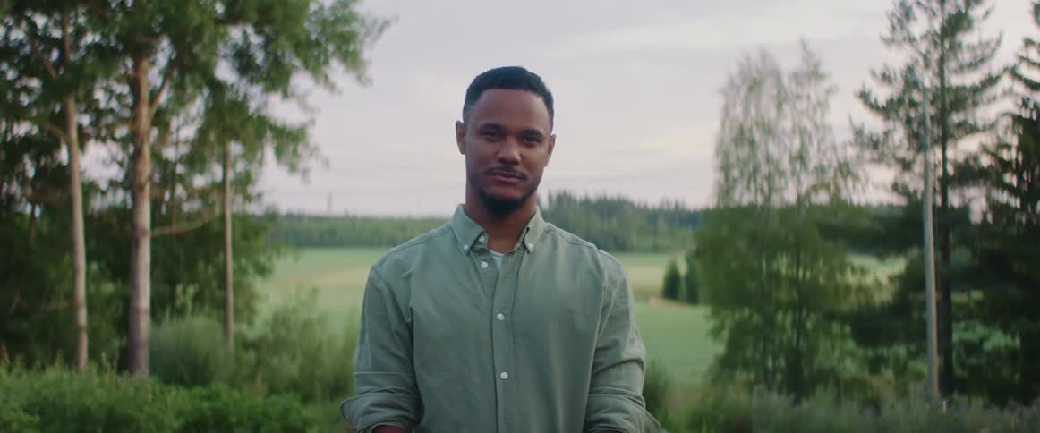Young man wearing green shirt looks at the camera standing near a field