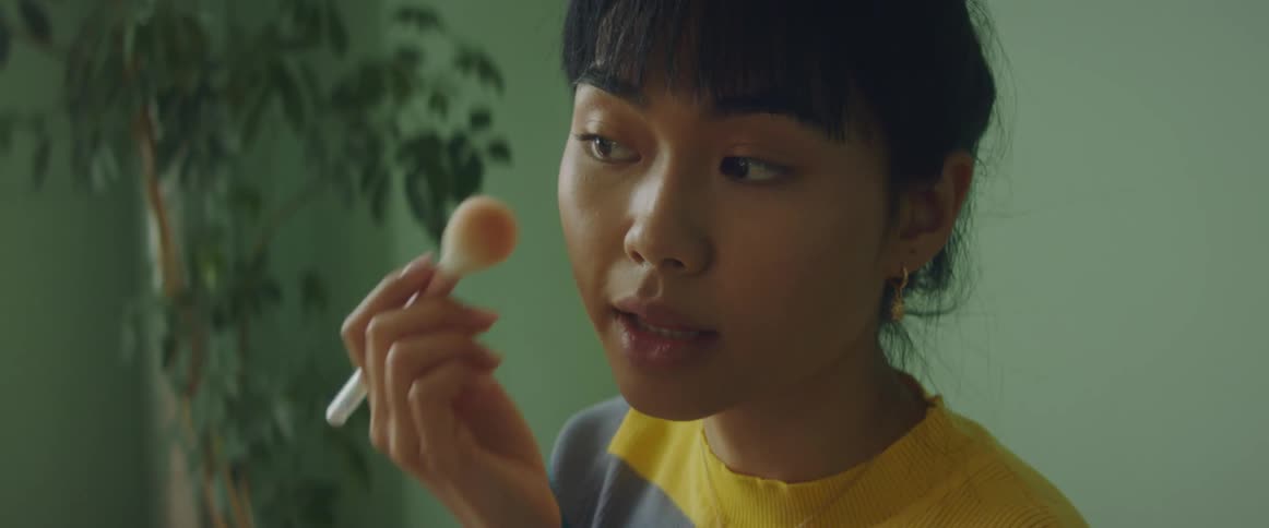 A woman carefully applies blush with a brush and talks to herself