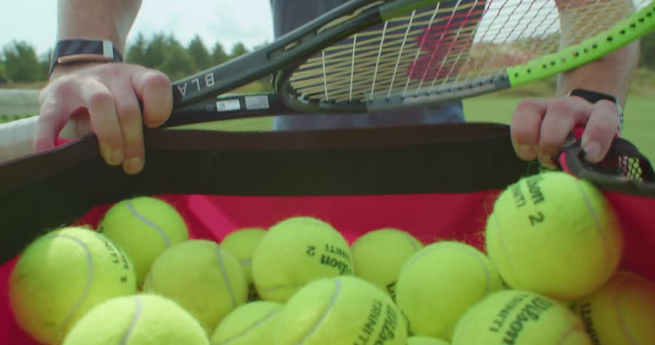 A man is pushing a cart full of tennis balls