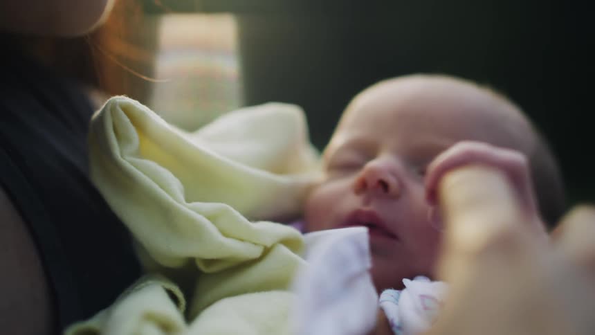 Newborn baby grabs her mother finger wrapped in a yellow blanket