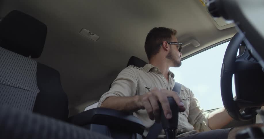 Man with sunglasses and stubble beard starts the car and drives away