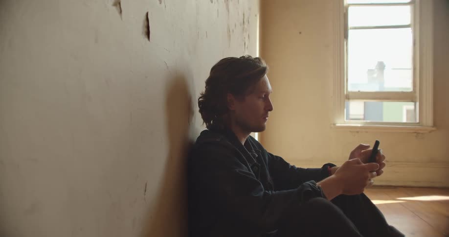 A man texts on his smartphone while sitting on the floor of an empty room