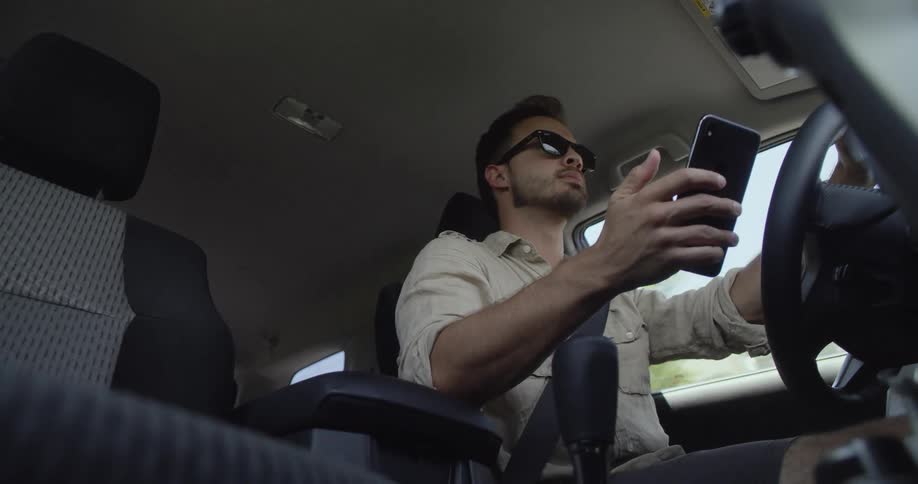 Man driving car scrolls and touches his mobile phone as he navigates