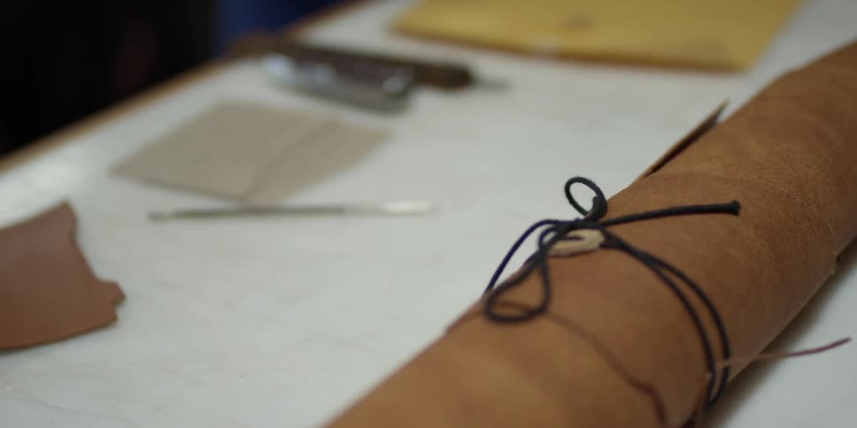 Someone working on a table strew with leather-working supplies