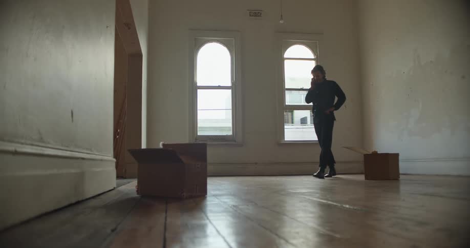 Man walking over the hardwood floor of an empty apartment talking on the phone