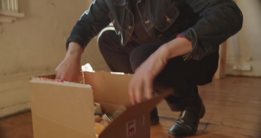 Young man unpacking a cardboard box inside an empty apartment
