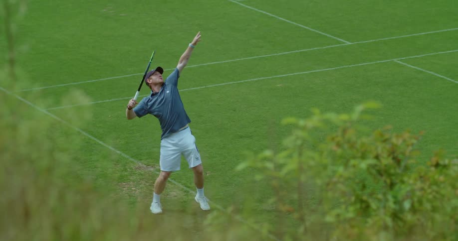 Man with cap blue shirt and and white shorts uses racket to hit tennis ball