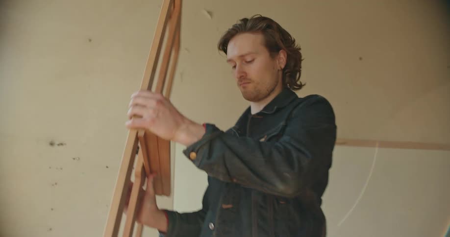 A man carries a wooden stand in to a room and sets it up