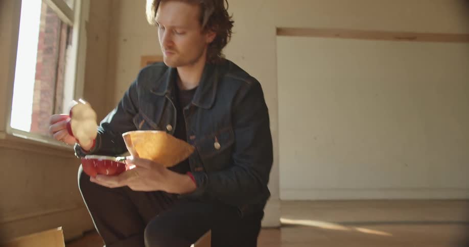 A man kneels on the floor packing a glass dish preparing to move