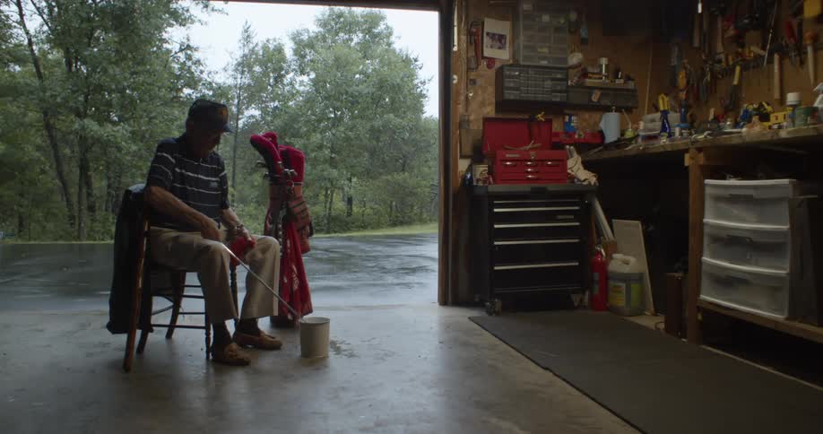 Man sits in chair in open garage cleaning golf club
