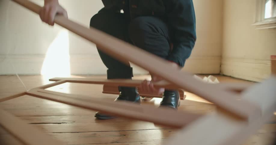 Man with denim jacket black pants sets up wooden easel in empty room