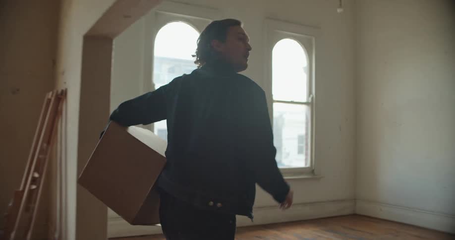 Man moving house carrying a cardboard box inside an empty apartment