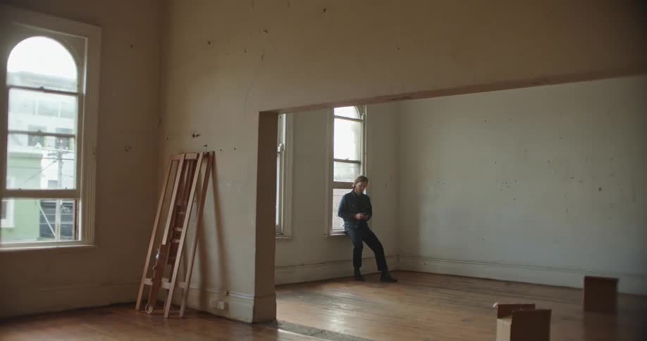 A man sits in an empty room by the window using a phone