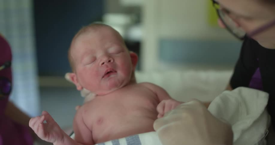 A nurse runs her hand down the face of a newborn to stimulate a crying reaction