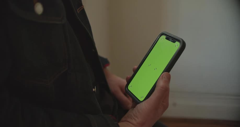 Man with denim jacket uses smartphone with green screen