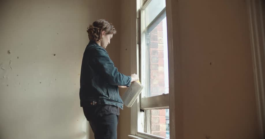 A man in a room measure in a window with a measuring tape with a wall in the background