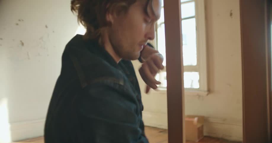 A man in a room standing up an easel with a wall and window in the background