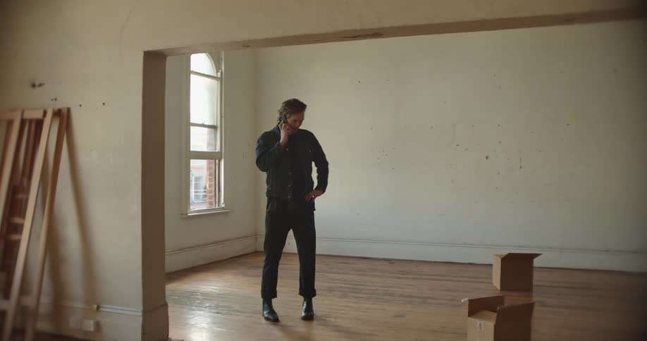 Man with denim jacket and pants talks on smartphone before moving in new house
