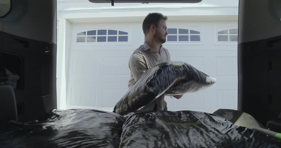 A man unloads bags of mulch from the bag of a vehicle