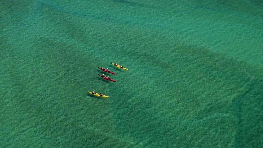 A group of tandem kayaks race across a lake during the day