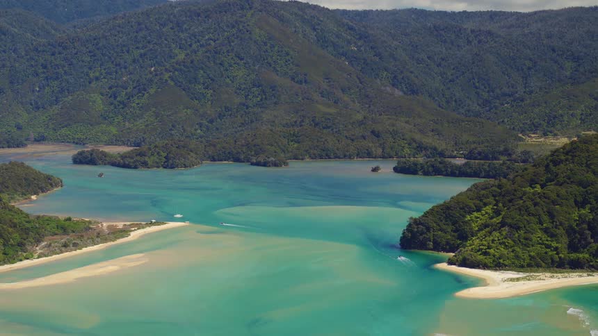 Aquamarine water contrasts with beach sand bordering forest covered mountains