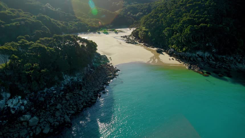 Clear blue water rolling in on beach surrounded by forested mountains
