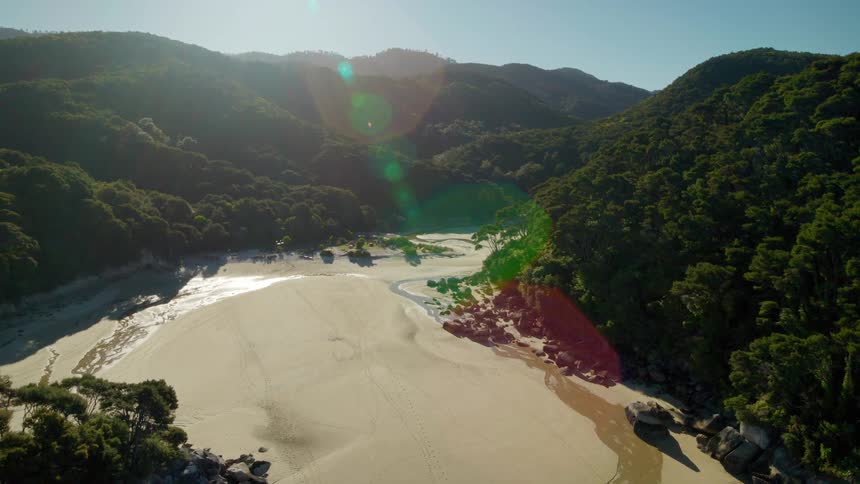 Waves rolling in on a beach surrounded by mountain forests on a sunny day